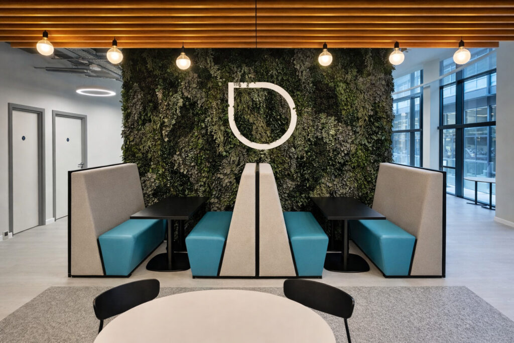 Office breakout area with modular seating and tables against a green wall