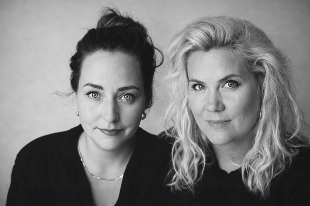 Two women, one with dark hair and one with blonde, looking at the camera